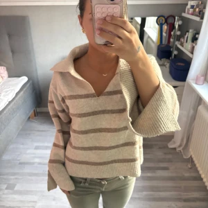Beige randig stickad tröja med krage - Supermysig stickad tröja i beige med breda bruna ränder och stor krage. Tröjan har v-ringning, vida ärmar och ribbade muddar. Tröjan är från GinaTricot och är knappt använd 🩷