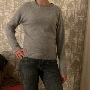Grå stickad tröja med rund hals VERO MODA - Enkel och stilren grå stickad tröja med rund halsringning och ribbade muddar vid ärmslut och nederkant. Långärmad modell som passar perfekt till jeans eller över en skjorta. Mjuk och skön känsla, perfekt för kyligare dagar. Strlk XS men känns som S/M