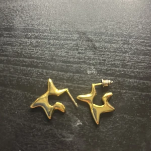 Unika guldiga örhängen i stjärnform - Säljer ett par coola örhängen i guldig metall med abstrakt stjärnformad design. De har en modern och edgy look som verkligen sticker ut. Perfekta för dig som vill ha något annorlunda och trendigt i smyckeskrinet. Från Edblad. Nypris 400kr nickelfria. Stainless steal