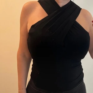 Svart omlott ärmlös topp H&M - Säljer en svart ärmlös topp från H&M med snygg omlott-detalj över bröstet och axlarna. Toppen har en tight passform och är gjord i mjuk bomull, perfekt för att lyfta vilken outfit som helst med sin coola design