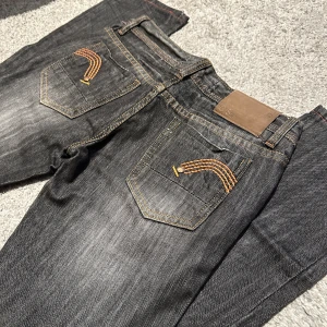  jeans från G-Star med brodyr - Snygga jeans från G-Star med orange broderad detalj på bakfickorna och läderpatch i midjan. Jeansen har klassisk femficksdesign, kontrastsömmar och rakt snitt. Innerbenslängd 72 cm. Midja - se bild. Storlek ca 27 eller 28.