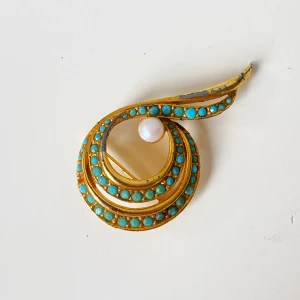 Vintage brosch i guld med turkosa stenar - Unik vintage brosch i spiralformad design med guldfärgad metall, dekorerad med små turkosa stenar och en vit pärla. Broschen har en cool retrovibe och är ca 5 cm lång. Perfekt för att ge din outfit en färgklick och personlig touch.