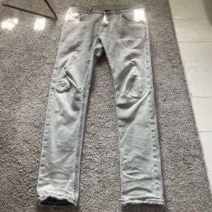 Grå slim fit jeans från dondup  - Snygga grå jeans från Dondup, modell mius slim fit. Jeansen har slitna detaljer vid knäna och bakfickorna, samt råa kanter vid bensluten. Klassisk femficksdesign och svart kontrastsöm på bakfickorna. Perfekta för en avslappnad streetstil. Dom är små i storleken, jag är 184 och dom är lite för små för mig. 