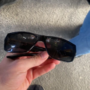 Svarta rektangulära solglasögon - Snygga svarta solglasögon med rektangulära bågar och mörka glas. Perfekta för att ge en cool vibe till din outfit. Bågarna är i plast och har en stilren, modern look.