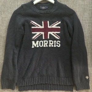 Mörkblå stickad tröja från Morris - Snygg mörkblå stickad tröja från Morris med Union Jack-flagga och logga framtill. Tröjan har ribbade muddar och rund hals. 