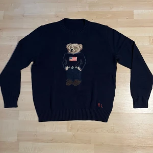 Mörkblå stickad tröja Polo Bear RL - Mörkblå stickad tröja från Ralph Lauren med ikoniska Polo Bear-motivet framtill. Tröjan har rund hals, långa ärmar och RL-broderi nertill. Perfekt för dig som gillar klassisk preppy stil med en twist. Oanvänd, pris kan diskuteras. Lapparna i nacken saknas 