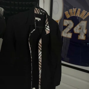 Svart Burberry skjorta XXL - Svart skjorta från Burberry i storlek XXL men asså den passar mer som s eller M lång ifrån XXL skulle inte ens säga att den ǎr L. Jag är 180 och väger 64 och den passar perfekt. med klassiskt rutigt mönster på insidan av kragen och knappslån. Skjortan har broderad Burberry-logga på bröstet och är långärmad. Snygg och stilren design som sticker ut med de rutiga detaljerna.