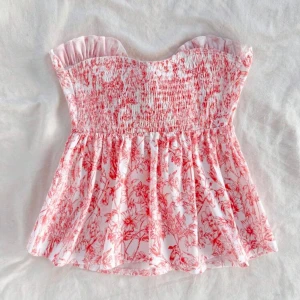 Blommig bandeau topp med rosett - Supersöt bandeau topp med orangeblommigt mönster. Volangkant upptill, stor knytrosett framtill. Helt slutsåld på hemsidan. 