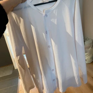 Vit kofta med knappar, storlek M - Enkel och stilren vit kofta i mjuk bomull med rund halsringning och knäppning framtill. Långärmad modell som passar perfekt till lager-på-lager. Snygg att slänga över en t-shirt eller linne för en clean look.