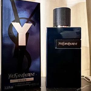 Yves Saint Laurent Y L'Elixir 100ml - Y L'Elixir från Yves Saint Laurent är en elegant parfym i en mörkblå, stilren glasflaska med svart metallock och tydlig logga. Flaskan rymmer 100 ml och har en lyxig känsla, perfekt för dig som gillar exklusiva dofter och snygg design.