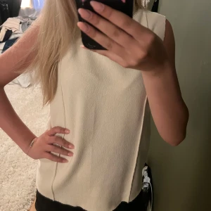 Beige ärmlös polotopp i stickat - Säljer en beige ärmlös polotopp i stickat material. Toppen har en hög ribbad krage och raka linjer längs sidorna. Passar snyggt till både jeans och kjol. storlek M men passar mig som vanligtvis är XS/S.