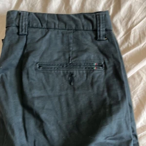 Svarta kostymbyxor med detalj - Snygga svarta kostymbyxor med raka ben och diskret fickdetalj med små gröna och röda sömmar. Byxorna har hällor för bälte och klassisk passform, perfekta för en clean och stilren look.