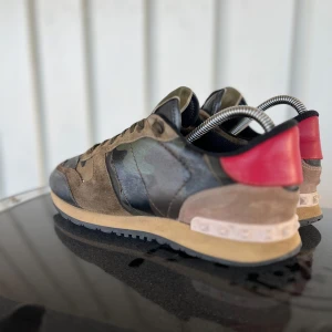 Valentino Garavani Rockrunner sneakers - Snygga Valentino Garavani Rockrunner sneakers i camomönster med detaljer i mocka, skinn och textil. Färgerna går i grönt, brunt, svart och rött med coola nitar på hälen. Perfekta för dig som vill sticka ut med lyxiga och trendiga sneakers. Har inte bråttom att sälja så ni behöver inte ens tänka på att ge skambud. Skick 8/10