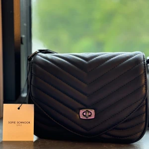 Svart quiltad axelväska Sofie Schnoor - Helt ny stilren svart axelväska från Sofie schnoor.Nypris 579 säljer för 380 . Väskan har ett  silverfärgat spänne framtill och justerbar axelrem.
