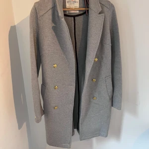 Grå kavajjacka Holly & Whyte XS - Snygg grå kavajjacka från Holly & Whyte by Lindex i storlek XS. Jackan har dubbelknäppning med guldiga knappar, klassisk krage och två fickor framtill. Perfekt för dig som vill ha en stilren och trendig look.