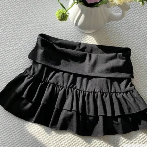 Svart volangkjol med bred midja - Vika ner kjol med inbyggda shorts, storlek m men snarare xs/s. Supersöt svart kortkjol med bred midjeresår och dubbla volanger. Kjolen har en flowy känsla och passar perfekt till en cool streetstyle-look. Enkel att matcha med crop tops eller hoodies för en trendig vibe.