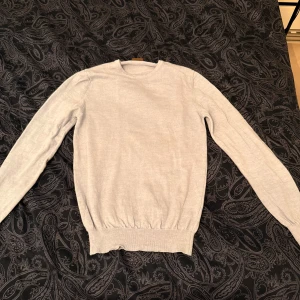 Ljusgrå/blå stickad tröja med armbågslappar - Snygg ljusgrå/blå stickad tröja från Stenströms i storlek M. Tröjan har rund hals, långa ärmar och matchande armbågslappar som ger en stilren touch. Perfekt för lager-på-lager och funkar året runt. Supermjuk och enkel att styla till jeans eller kjol.