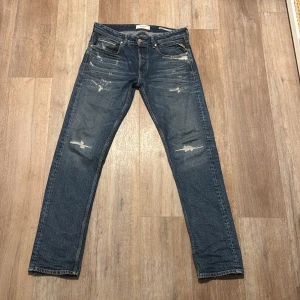 Replay Grover blå jeans straight fit - Säljer ett par Replay Grover jeans i klassisk blå tvätt med slitna detaljer och raka ben. Jeansen har fem fickor, knäppning med knappar och snygga kontrastsömmar. Perfekta för en avslappnad och cool look.