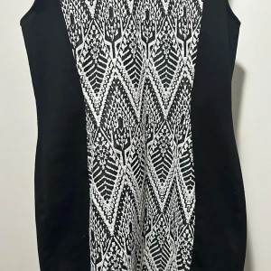 Svartvit mönstrad kortklänning - Snygg svart klänning med vit grafisk mönsterpanel framtill. Ärmlös och figurnära modell som ger en cool och modern look. Perfekt för dig som gillar kontraster och unika detaljer. Materialet känns mjukt och följsamt. Den ser mycket bättre på än bara bilden!🩷