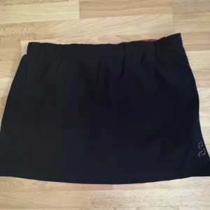 Ny. Svart träningskjol från Crivit Sports - Svart sportig kortkjol från Crivit Sports med inbyggda shorts under. Kjolen har elastisk midja och diskret logga nertill. Perfekt för dig som vill ha en bekväm och stilren look till träningen.