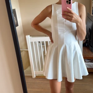 Vit kort klänning med utsvängd kjol - Supersöt vit kort klänning med ärmlös design och rund halsringning. Klänningen har en figurnära överdel och en utsvängd kjol som ger en riktigt snygg siluett. Materialet är slätt och i god kvalité. 