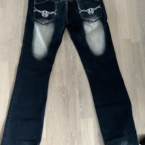 Blue Queen jeans med brodyr och detaljer - Mörkblå jeans från Blue Queen med vita kontrastsömmar, broderade detaljer och dekorativa mönster på ben och bakfickor. Snyggt slitna partier framtill och broderad logga på ficka och linning. Klassisk femficksmodell i jeansmaterial.