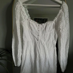 Vit broderad kortklänning med långa ärmar - Superfin vit kortklänning med broderade detaljer och långa puffärmar. Klänningen har en söt v-ringning och knappar framtill. Perfekt till student eller sommarens festligheter! Storlek 38 men passa mig som vanligtvis har 36. Kan skicka fler bilder om intresserad