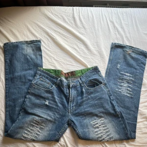 Blå slitna jeans från Portland State - Säljer ett par blå jeans från Portland State med slitna detaljer på både fram- och baksida. Jeansen har klassisk femficksdesign, raka ben och normal passform. Perfekta för en avslappnad och trendig look. Jeansen är mid/low waist och är lite sliten som ni ser på bilderna 