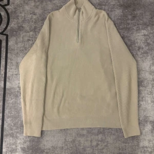 Beige tröja från ONLY & SONS - Säljer en beige ribbad tröja från ONLY & SONS med halv dragkedja och hög krage. Tröjan har lång ärm och är tillverkad i ett mjukt material som passar perfekt för lager-på-lager-stil.