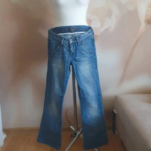 Blå jeansbyxor från Cross - Säljer ett par klassiska blå jeansbyxor från Cross med normal passform. Byxorna har fem fickor, knappgylf och snygga slitningar för en avslappnad look. Bakfickorna har dekorativa sömmar och läderpatch med logga.