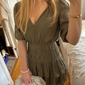 Olivgrön omlottklänning från Maje - Supersöt grön kortklänning från Maje med v-ringning och knyt vid halsen. Klänningen har volangdetaljer, korta puffärmar och ribbad midja som ger en fin siluett. Perfekt för vår och sommar! Volangklänning, miniklänning, sommarklänning, kärt barn har många namn lol. Storleken motsvarar en s / xs . Köpt i Frankrike. Slutsåld! Nyskick!  Hör gärna av er vid frågor 💕💕😇😇😇🙌