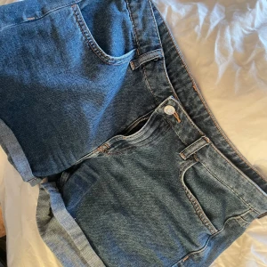 Blå jeansshorts Regular Waist - Säljer ett par klassiska blå jeansshorts med regular waist och femficksmodell. Shortsen har uppvikta benslut och stängs med dragkedja och knapp. Perfekta för varma dagar och enkel att matcha med olika toppar.