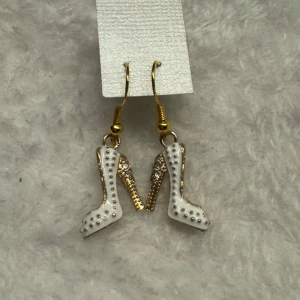 Örhängen med vita högklackade skor - Unika örhängen i form av vita högklackade skor med gulddetaljer och små glittriga stenar. Perfekt accessoar för dig som vill sticka ut och addera lite glamour till din stil.. krokarna är i sterling silver 