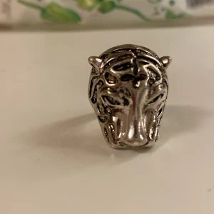 Silverfärgad ring med tigerhuvud - Cool ring i silverfärg med ett detaljerat tigerhuvud framtill. Ringen har en bred design och passar perfekt för dig som vill sticka ut med ett djurinspirerat smycke.