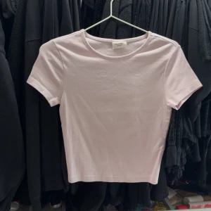 Ljusrosa croppad t-shirt - Säljer en ljusrosa croppad t-shirt med rund halsringning och korta ärmar. Perfekt basplagg att matcha med jeans eller kjol. Enkel och stilren design.