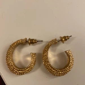 Guldiga creolörhängen med struktur - Säljer ett par snygga guldiga creolörhängen med cool bubblig struktur. Perfekta för att lyfta vilken outfit som helst! Stift och lås i samma färg. Passar dig som gillar statement-smycken.