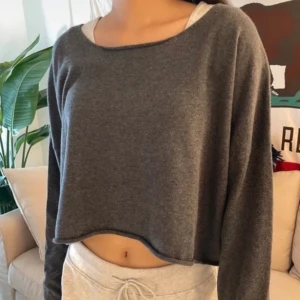 Mörkgrå croppad brandy melville tröja  - Säljer en enkel och stilren mörkgrå croppad tröja med rund halsringning och långa ärmar. Perfekt för en avslappnad look och lätt att matcha med olika outfits.