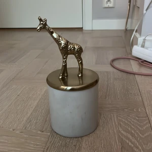 Vit burk med mässingslock och giraff - Snygg vit burk i marmor med lock i mässing och en dekorativ giraff på toppen. Perfekt som accessoar till rummet för att förvara småsaker eller smycken. Ger en lyxig känsla med sin kombination av marmor och metall.