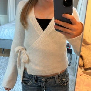 Vit omlottstickad tröja från Gina Tricot - Superfin vit stickad omlott-tröja från Gina Tricot i ullblandning. Tröjan har långa ärmar, knyt i sidan och ribbade muddar. Perfekt att styla med jeans eller kjol för en fin outfit