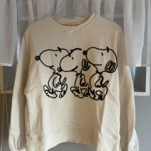 Vit sweatshirt med Snoopy-tryck från Zara x Peanuts - Vit sweatshirt från Zara i samarbete med Peanuts, med stort svart tryck av Snoopy på framsidan. Tröjan har rund halsringning och långa ärmar.