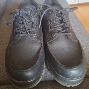 Svarta läderskor från Ecco med snörning - Klassiska svarta läderskor från Ecco med robust sula och snörning. Skorna har rund tå och är märkta med Gore-Tex för extra vattentålighet. Perfekta för dig som vill ha bekväma och stilrena skor till vardags. Använde de en gång och sedan var den för stor.