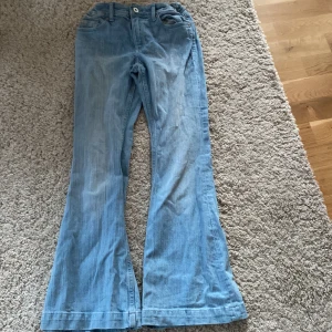 Ljusblå bootcut jeansbyxor - Säljer ett par ljusblå jeansbyxor med bootcut passform. Byxorna har klassiska fickor både fram och bak samt stängs med knapp och dragkedja. Perfekta för dig som gillar en trendig look.