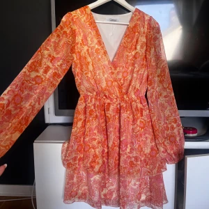 Blommig orange och rosa omlottklänning - Säljer en superfin kortklänning med blommigt mönster i orange och rosa färger. Perfekt till stundentmotagning/ firanden, midsommar eller en vanlig sommar dag🌺