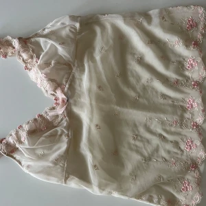 Beige spetslinne med rosett och broderade blommor - Säljer ett romantiskt beige linne med spetskant, små broderade blommor i rosa och en söt rosett framtill. Tunt och lätt material, perfekt för lager-på-lager eller som ett statement-plagg. I storlek s/m. Pris kan diskuteras💗