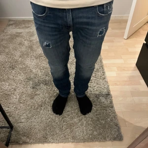 Blå Replay jeans med slitningar - Säljer ett par blå jeans från Replay med slitna detaljer. Storlek är 30:30. Säljer dom på grund av att de inte kommer till så stor användning längre.
