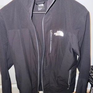 Svart jacka från The North Face med luva - Säljer en svart jacka från The North Face med luva och dragkedja framtill. Jackan har två sidofickor med dragkedja och logga på bröstet samt ryggen.