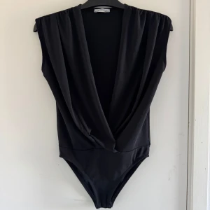 Svart omlott body  - Snygg svart omlott body från Zara Trafaluc. Den är ärmlös och har en djup v-ringning (katt och kanin finns i hemmet) 