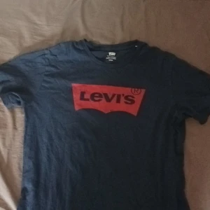 Blå t-shirt från Levi's - Säljer en klassisk blå t-shirt från Levi's med röd logga på bröstet. Tillverkad i 100% bomull för en skön och bekväm känsla. Perfekt för en avslappnad stil.