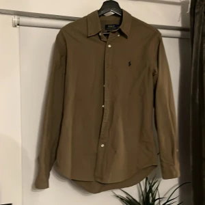 Brun skjorta från Polo Ralph Lauren - Säljer en stilren brun skjorta från Polo Ralph Lauren i slim fit. Skjortan har långa ärmar och knappar framtill. Perfekt för en elegant look.