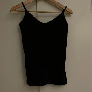 Svart linnetopp - Snygg svart linnetopp med smala axelband. Perfekt för lager-på-lager eller att bära som den är. Enkel och stilren design som passar till det mesta.